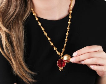 Peut inclure: Un collier en or avec un pendentif en forme de grenade. Le pendentif est ouvert pour révéler des joyaux rouges à l'intérieur.