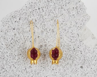 May include: A pair of gold earrings shaped like pomegranates with red gemstone accents.