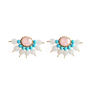 Op de afbeelding: Een paar gouden oorbellen met een roze edelsteen omringd door turquoise en witte kralen.