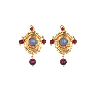May include: A pair of gold earrings with a blue stone center and red beads. The earrings have a circular design with a textured edge.