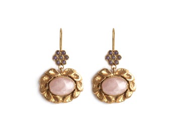 May include: Gold earrings with a pink oval gemstone surrounded by a textured gold design. The earrings have a small cluster of purple gemstones at the top.