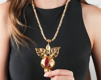 May include: A gold necklace with a pomegranate pendant. The pendant is detailed with red jewels and gold leaves.