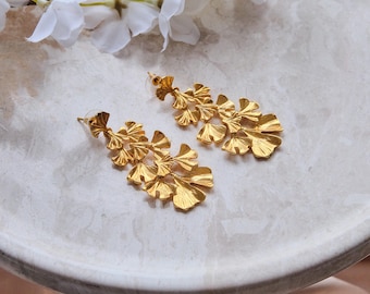 May include: A pair of gold-tone dangle earrings with a leaf design. The earrings are made of multiple overlapping leaves, creating a cascading effect.