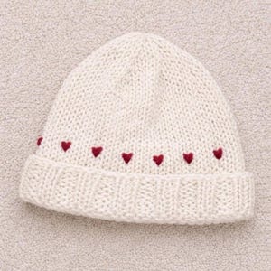 May include: Cream-colored knit beanie with a folded brim. The hat features a row of small, embroidered red hearts near the brim. The beanie is made of a soft, textured yarn, perfect for cold weather.