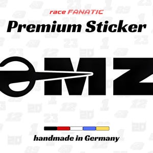Könnte beinhalten: Ein schwarzer "Premium Sticker" mit den Buchstaben "OMZ" in fetter Schrift. Der Aufkleber enthält den Text "race FANATIC" in Rot und "handmade in Germany" unter einem Farbbalken.