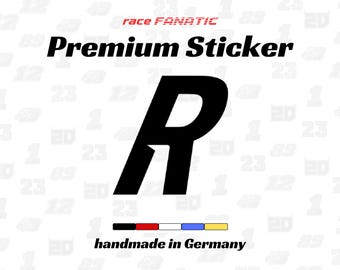 Könnte beinhalten: Ein schwarzer Aufkleber mit einem großen Buchstaben R in einer fetten, kursiven Schriftart. Über dem Buchstaben steht der Text race FANATIC Premium Sticker. Unter dem Buchstaben befindet sich eine Reihe von fünf kleinen farbigen Rechtecken und der Text handmade in Germany.