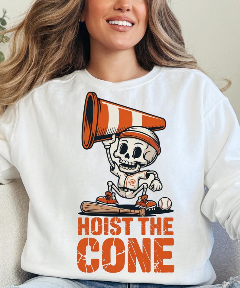 May include: White sweatshirt featuring a cartoon skeleton in a baseball uniform holding a traffic cone. The skeleton is standing on a baseball bat, with a baseball nearby. The text "HOIST THE CONE" is printed in orange.