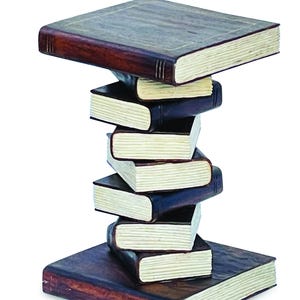 May include: A decorative side table constructed from a stack of seven books. The base and top are large, flat, dark brown books, while the central column consists of five smaller, staggered books with visible cream-coloured pages and dark spines.