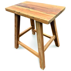 May include: A rectangular wooden stool featuring a natural light and dark brown wood grain pattern. The stool has four sturdy legs connected by horizontal support bars on all sides, with a thick, flat top surface showing visible wood texture.