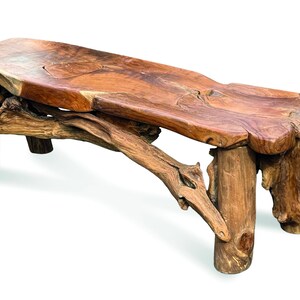 May include: A bench crafted from a single piece of natural wood with a polished, warm brown surface. The seat features organic, uneven edges and visible wood grain. It is supported by four thick, sturdy log legs and a decorative branch.