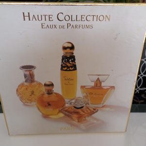 Puede incluir: Una caja blanca con ribetes dorados con el texto "Haute Collection Eaux de Parfums PARIS". La caja muestra imágenes de cinco frascos de perfume de varias formas, llenos de líquido color ámbar.