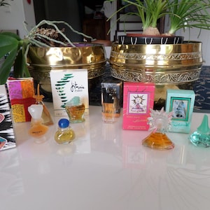 Peut inclure: Une collection de flacons de parfum miniatures et de boîtes de différentes formes et couleurs, dont un flacon en forme de femme et un flacon avec un bouchon bleu. Les boîtes présentent différents motifs et textes.