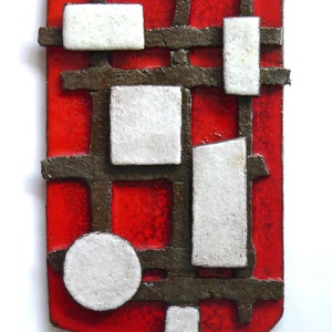 May include: A red ceramic wall sculpture with a geometric design. The sculpture features white squares and circles, and brown lines.