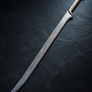 May include: A silver-toned sword featuring a curved blade with intricate, etched vine-like patterns running along the center. The hilt has a smooth, metallic finish with a flared pommel, and the design extends from the guard down the blade.