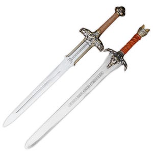 May include: Two decorative swords with metallic blades and intricate hilts. The top sword features a brown wrapped grip and a pommel with a skull design. The bottom sword has a reddish-brown wrapped grip and a crossguard shaped like a skull.