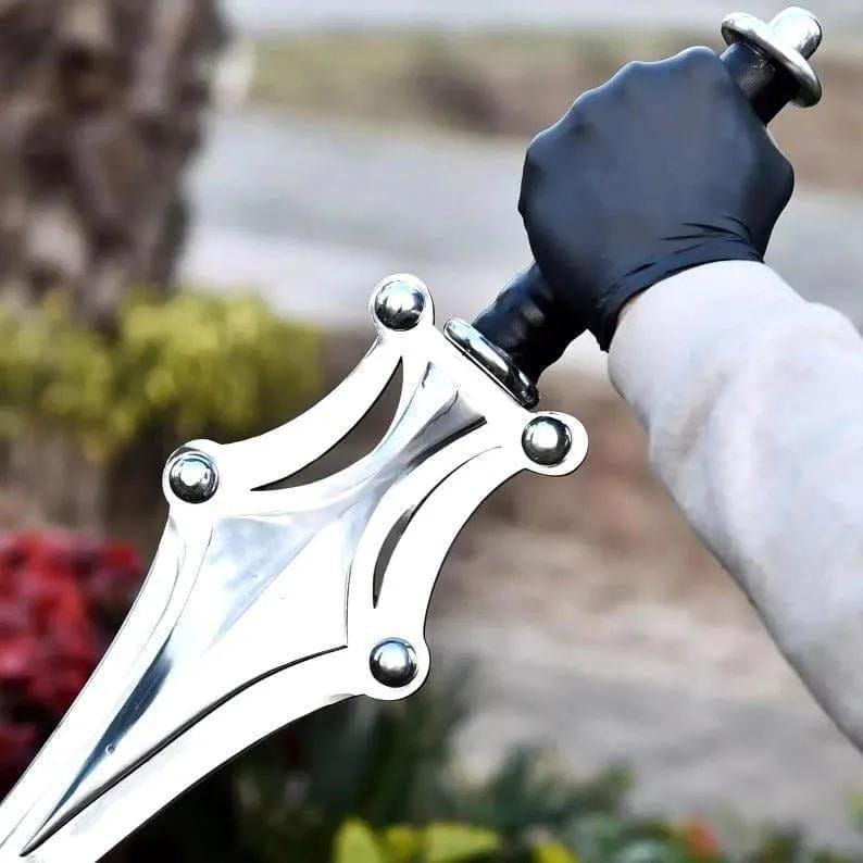Op de afbeelding: Een zilverkleurige metalen dolk met een breed, puntig lemmet met decoratieve uitsparingen en vier opvallende ronde klinknagels. Het handvat is zwart met een metalen pommel, vastgehouden door een hand met een zwarte handschoen.