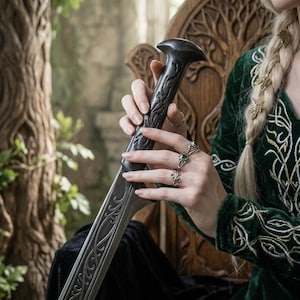 May include: A long sword with a dark, ornate handle featuring intricate carvings and a metallic blade with decorative engravings. The sword is held by fingers adorned with three silver rings, each set with a small green stone, and a thin silver band.