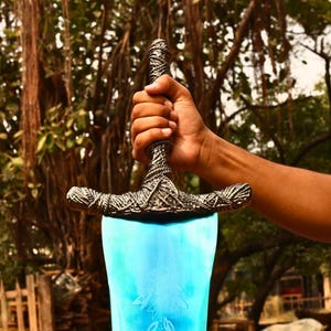 May include: A sword with a bright blue blade featuring an etched leaf pattern and a textured, dark metallic hilt with intricate rope-like detailing. The crossguard is wide and curved, matching the weathered, antique-style finish of the handle.