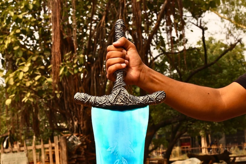 May include: A sword with a bright blue blade featuring an etched leaf pattern and a textured, dark metallic hilt with intricate rope-like detailing. The crossguard is wide and curved, matching the weathered, antique-style finish of the handle.