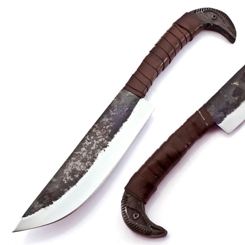 May include: Hand-forged knife with a dark, textured blade and a brown leather-wrapped handle. The handle features a decorative bird's head design at the end. The knife is designed for cutting and chopping.