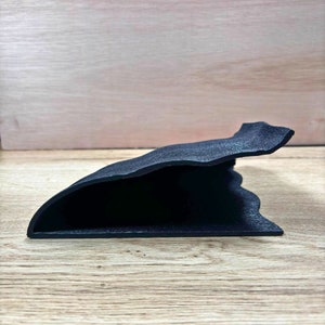 Pu&ograve; includere: Un vassoio decorativo nero e strutturato con una forma organica unica. Il vassoio ha un design curvo con un bordo rialzato e poggia su una superficie in legno. Il vassoio &egrave; lungo circa 25 cm.