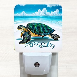May include: A white night light with a colorful image of a sea turtle swimming in the ocean. The image has a blue sky with white clouds and the text "Stay Salty".