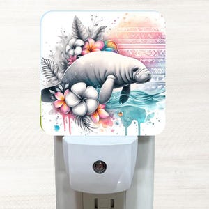 May include: A watercolor illustration of a manatee swimming in a turquoise ocean with pink and white flowers. The image is on a white nightlight plug-in.