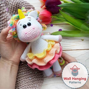 May include: A handmade crochet unicorn doll with a white body, a yellow horn, and a colorful mane. The doll wears a layered skirt in shades of yellow, orange, and pink. The doll is held in someone's hands.