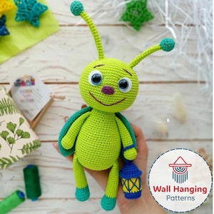 Puede incluir: Muñeca de ganchillo verde hecha a mano con grandes ojos azules, nariz morada y boca sonriente. La muñeca tiene alas azules y verdes y sostiene una linterna azul y amarilla. Un artículo artesanal caprichoso.