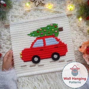 Puede incluir: Colgante de pared de ganchillo blanco con un coche rojo con un árbol de Navidad verde encima. El coche tiene ventanas azules y ruedas negras. El colgante tiene flecos en la parte inferior y una clavija de madera en la parte superior.