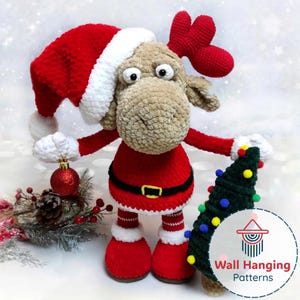 May include: A handmade, plush Christmas reindeer wearing a Santa hat and suit, holding a small Christmas tree and a red ornament. The reindeer is brown, red, and white, with a black belt and a gold buckle. The Christmas tree is green with colorful lights.