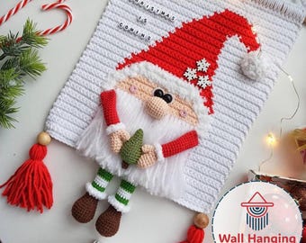 May include: Crocheted Christmas wall hanging featuring a Santa Claus design. The Santa has a red hat, white beard, and holds a small green tree. The wall hanging is white with the text "CHRISTMAS IS COMING". Red tassels and a candy cane are also visible.