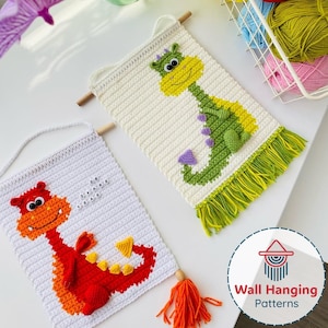 May include: Two handmade crochet wall hangings featuring dragon designs. One dragon is red and orange, the other is green and yellow. Both hangings have a white background, wooden dowels, and fringe. The red dragon has the text "38 YEARS BRAVE".