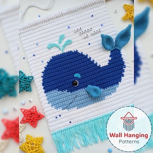 Puede incluir: Un tapiz de pared de ganchillo hecho a mano con un diseño de ballena azul. La ballena está sobre un fondo blanco con detalles en azul y el texto "THE OCEAN IS LOVE". El tapiz tiene una franja en la parte inferior y está decorado con estrellas.