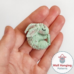 May include: A small, crocheted bunny in a sleeping pose. The bunny is light green with pink accents on the ears and is embellished with small, silver-colored beads. The bunny is approximately 2 inches long.