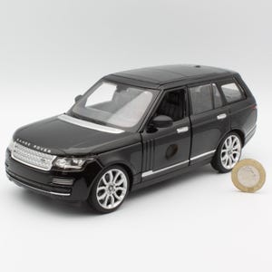 May include: A black Range Rover model car with silver trim and detailed wheels. The model is a miniature replica of the luxury SUV. A coin is placed next to the car for size comparison.