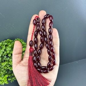 May include: A dark red prayer beads or rosary with a tassel. The beads are oval shaped and strung on a red cord.