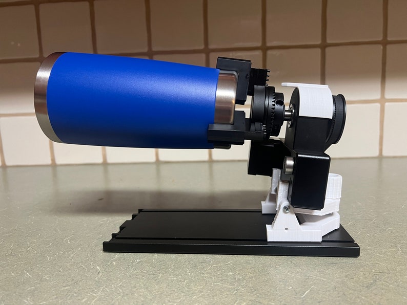 Peut inclure: Un gobelet bleu est mont&eacute; sur un dispositif imprim&eacute; en 3D noir et blanc. Le dispositif est dot&eacute; d'un petit moteur et d'un syst&egrave;me d'engrenages. Le dispositif est mont&eacute; sur une base noire.