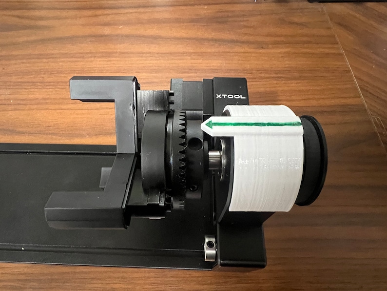 Peut inclure: Gros plan sur une imprimante 3D noire et blanche avec une bobine de filament blanc. La bobine est &eacute;tiquet&eacute;e "XTOOL" et une fl&egrave;che verte indique la direction d'alimentation du filament.