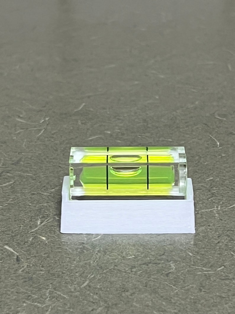Peut inclure: Un niveau en plastique blanc avec un niveau &agrave; bulle en verre transparent. Le niveau &agrave; bulle est vert et comporte une ligne noire au centre.