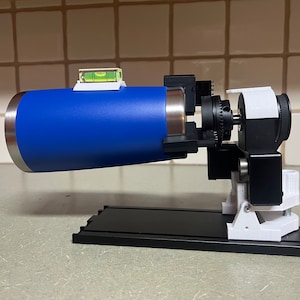 Peut inclure: Un objet cylindrique bleu mont&eacute; sur une base noire avec des supports blancs. L'objet a un niveau fix&eacute; au sommet et un petit moteur noir sur le c&ocirc;t&eacute;.