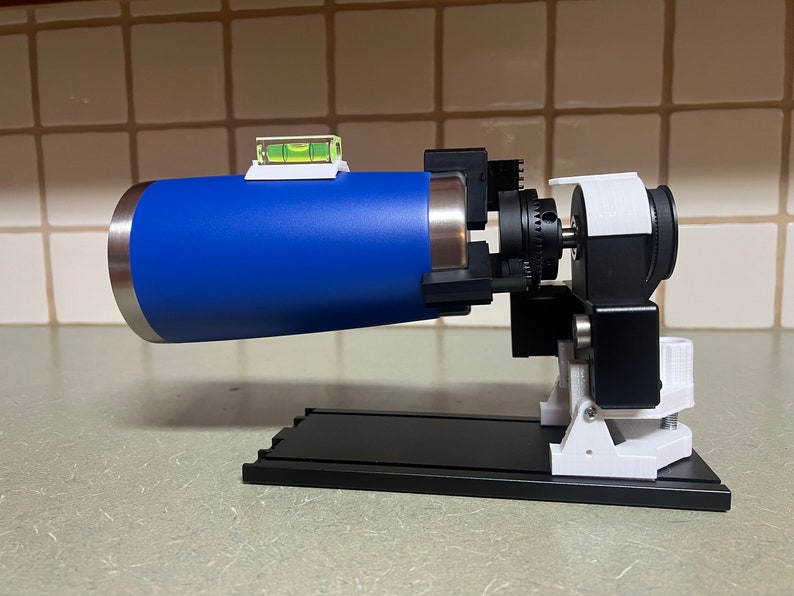 Peut inclure: Un objet cylindrique bleu mont&eacute; sur une base noire avec des supports blancs. L'objet a un niveau fix&eacute; au sommet et un petit moteur noir sur le c&ocirc;t&eacute;.