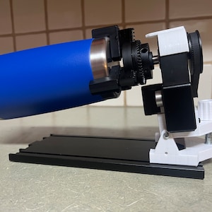 Peut inclure: Un dispositif imprim&eacute; en 3D avec une bouteille d'eau bleue fix&eacute;e &agrave; un m&eacute;canisme rotatif. Le dispositif est mont&eacute; sur une base noire avec une pince blanche.