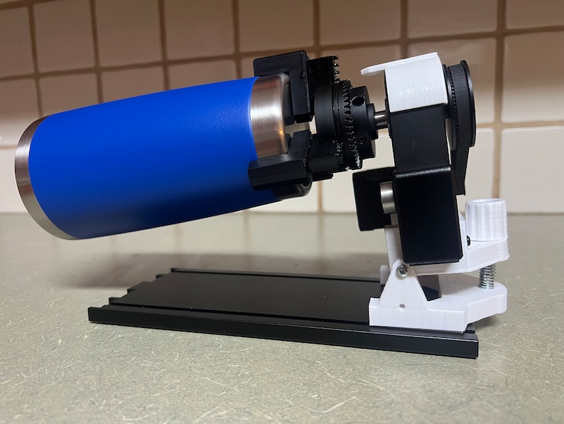 Peut inclure: Un dispositif imprim&eacute; en 3D avec une bouteille d'eau bleue fix&eacute;e &agrave; un m&eacute;canisme rotatif. Le dispositif est mont&eacute; sur une base noire avec une pince blanche.