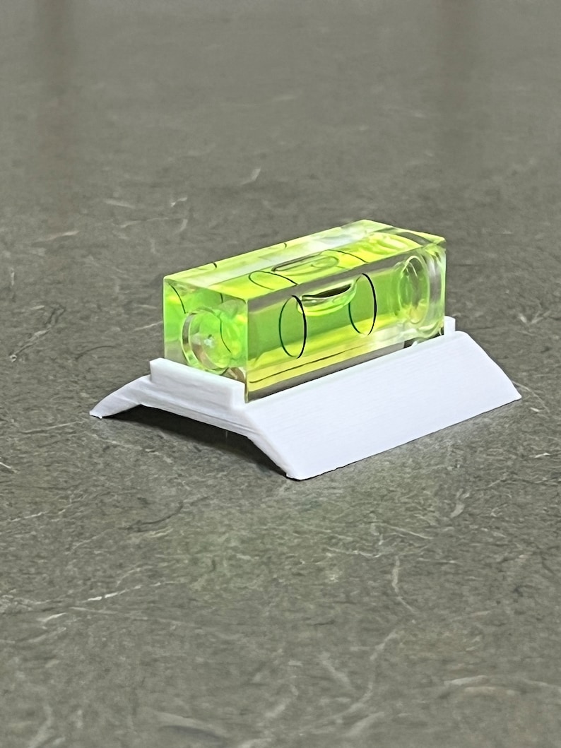 Peut inclure: Un petit niveau en plastique transparent avec un liquide vert &agrave; l'int&eacute;rieur. Le niveau est mont&eacute; sur une base en plastique blanc.