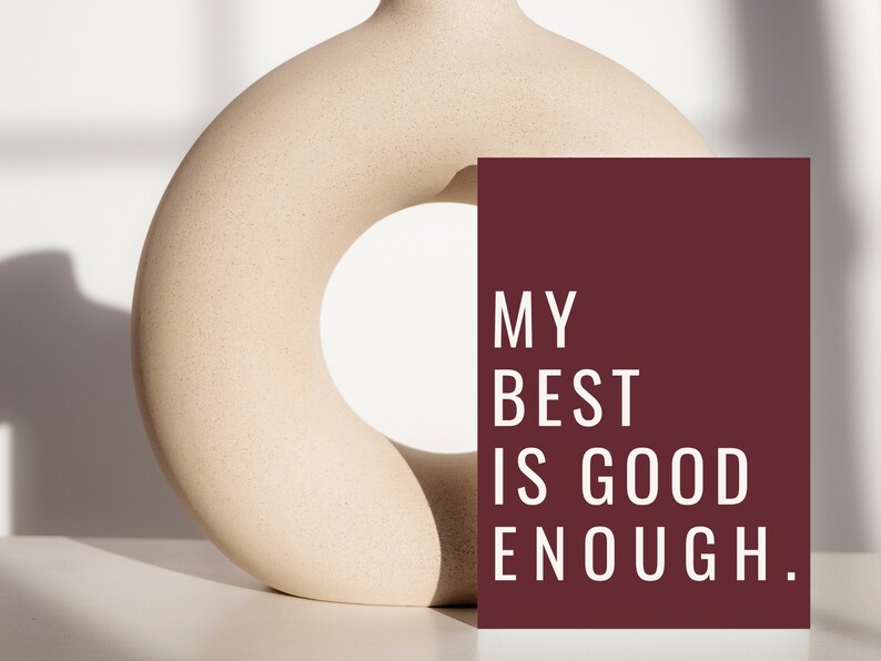 Może przedstawiać: Burgundowa karta z białym tekstem, kt&oacute;ry brzmi "MY BEST IS GOOD ENOUGH." Karta opiera się o beżowy ceramiczny wazon z dużym otworem w środku.