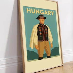 May include: Framed poster featuring a stylized illustration of a person in traditional Hungarian attire. The poster has the word "HUNGARY" at the top. The person is wearing a black vest with floral embroidery, a white cape, and a black hat.