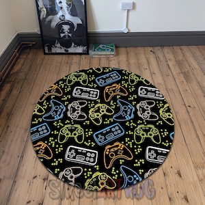 Peut inclure: Un tapis rond noir avec un motif répété de manettes de jeu vidéo aux couleurs néon. Les manettes sont soulignées en blanc, bleu, orange et jaune. Le tapis est posé sur un plancher en bois.