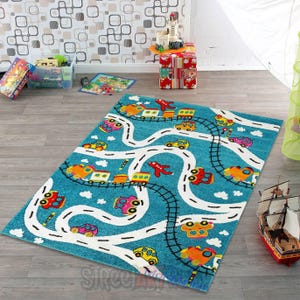 May include: A rectangular, turquoise children's rug featuring a road and railway design with colorful cars, trains, and airplanes. White roads and black railway tracks wind across the rug, with playful illustrations of vehicles.