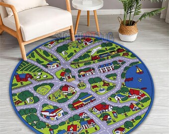 May include: A round children's play rug featuring a town map design. The rug has a blue border and depicts roads, houses, trees, a farm, and a lake with a sailboat. The color palette includes green, purple, red, and blue.